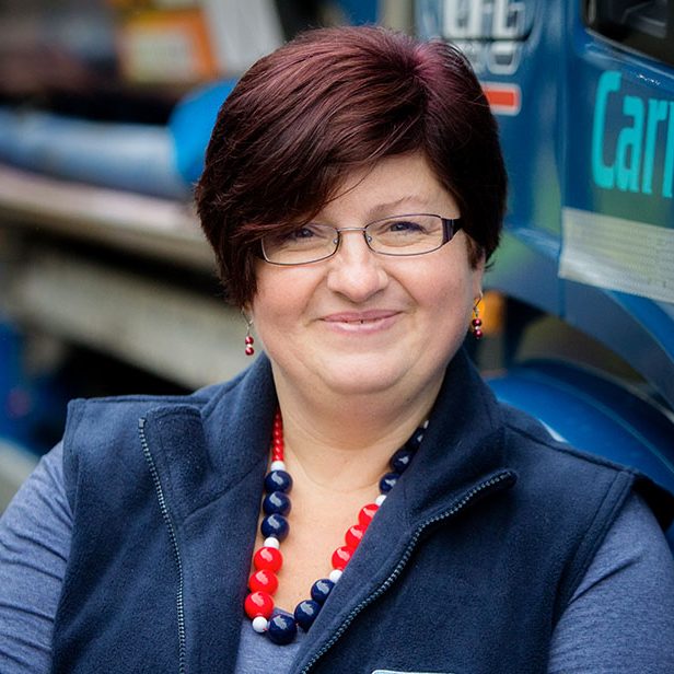 Professional head shot of Rosie Carnegie standing in front of a Carnegie Fuels truck and wearing a branded Carnegie Fuels gilet.