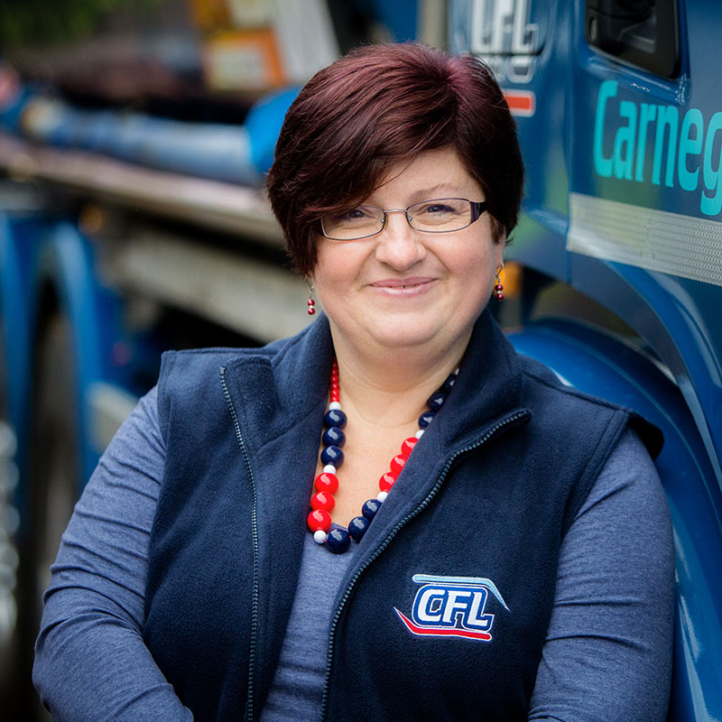 Professional head shot of Rosie Carnegie standing in front of a Carnegie Fuels truck and wearing a branded Carnegie Fuels gilet.