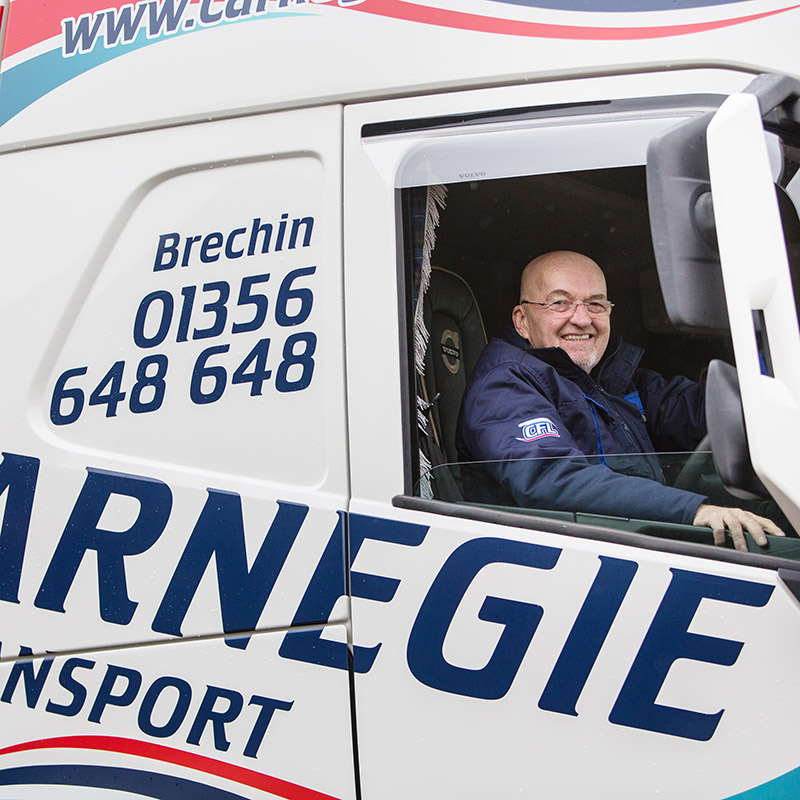 close up of a man with glasses sitting in the cab of a Carnegie Transport lorry with the driver's side window down