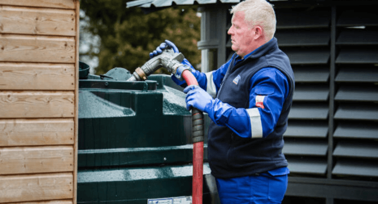 A Carnegie Fuels employee putting domestic oil into an outdoor home oil tank through a fuel hose.